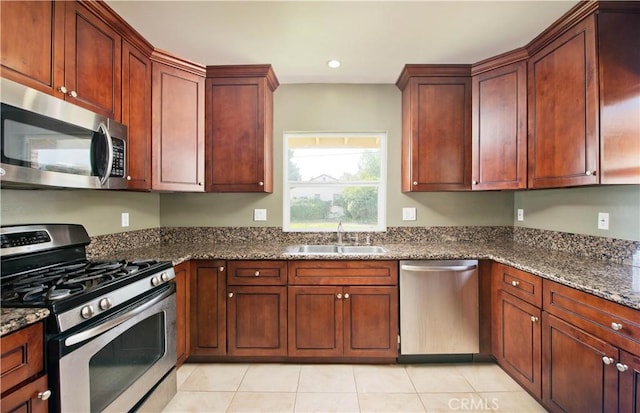 kitchen featuring stainless steel appliances, recessed lighting, dark stone countertops, a sink, and light tile patterned floors