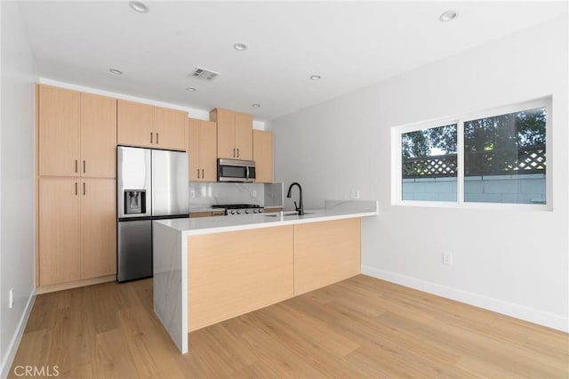 kitchen featuring visible vents, a peninsula, light brown cabinetry, light wood-type flooring, and appliances with stainless steel finishes