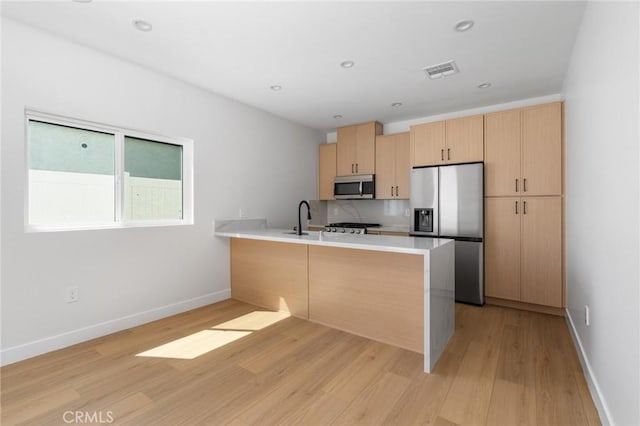 kitchen featuring light brown cabinetry, light wood finished floors, stainless steel appliances, a peninsula, and visible vents