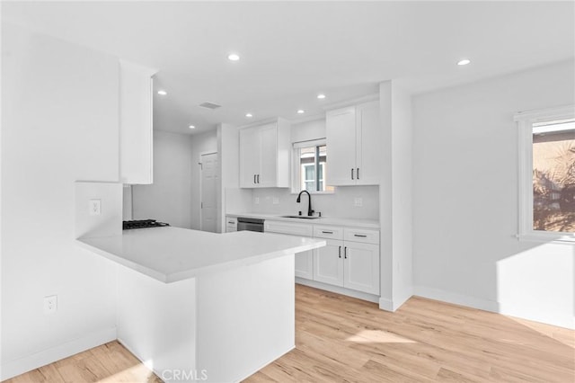 kitchen featuring baseboards, light countertops, white cabinets, a sink, and dishwasher