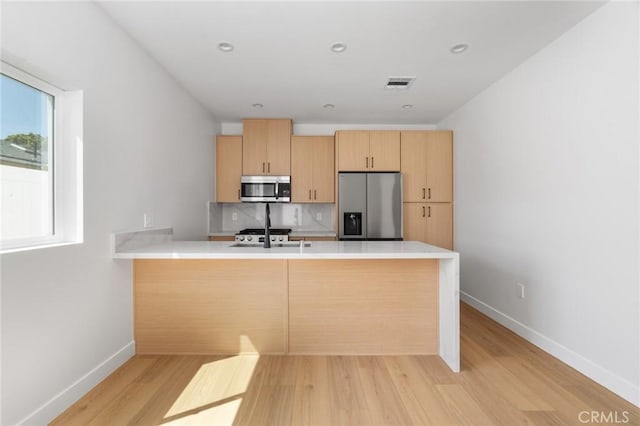 kitchen featuring visible vents, light brown cabinetry, appliances with stainless steel finishes, a peninsula, and light wood-style floors