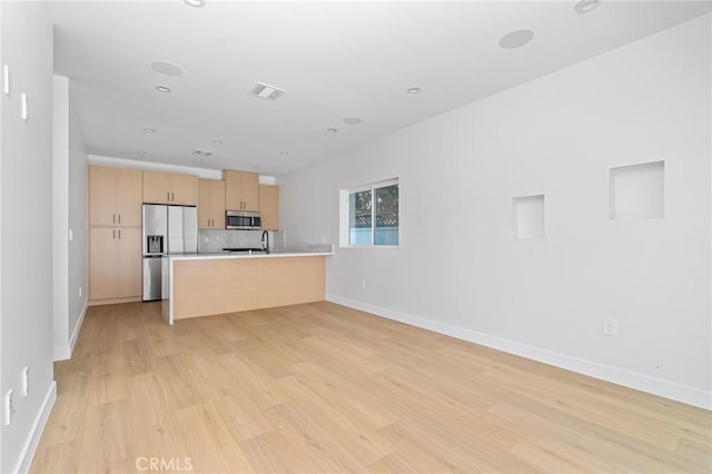 kitchen with light brown cabinets, light countertops, stainless steel appliances, light wood-type flooring, and visible vents