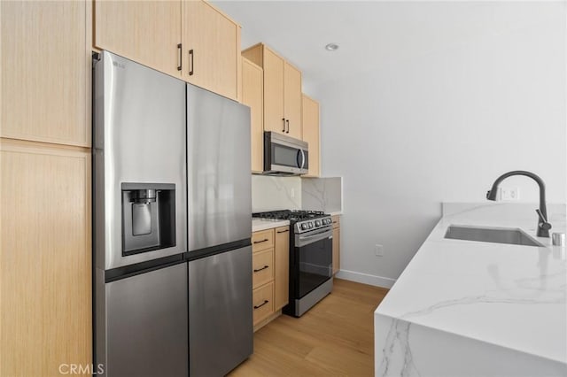 kitchen featuring light brown cabinetry, appliances with stainless steel finishes, a sink, baseboards, and light wood-type flooring