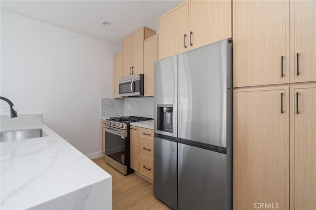 kitchen with light brown cabinetry, light stone countertops, a sink, light wood finished floors, and stainless steel appliances