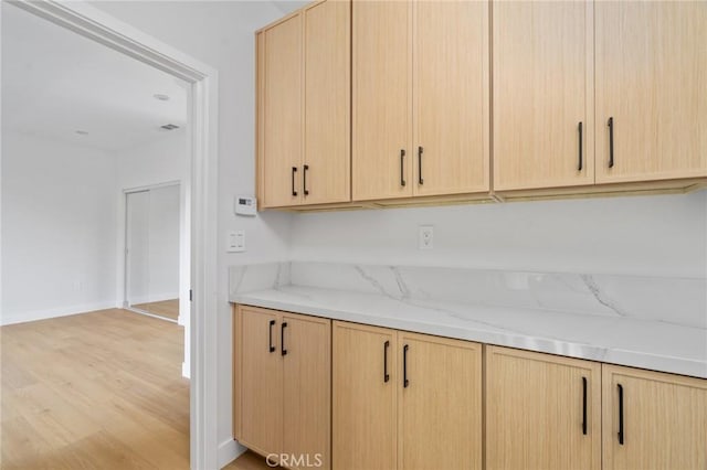 kitchen with light wood-style floors, baseboards, light stone counters, and light brown cabinets