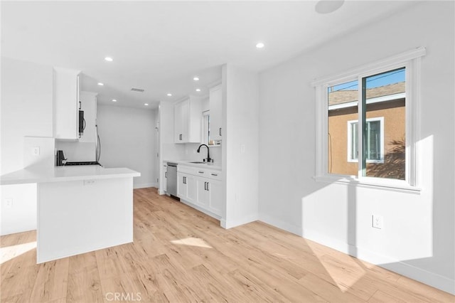 kitchen featuring white cabinets, a sink, light wood finished floors, dishwasher, and light countertops