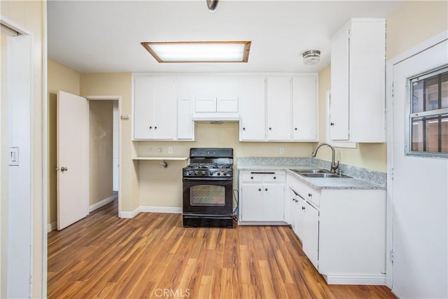 kitchen featuring light wood-type flooring, white cabinets, light countertops, a sink, and black gas range