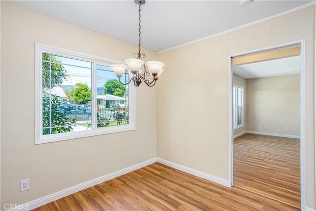 spare room with light wood-type flooring, an inviting chandelier, and baseboards