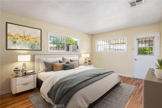 bedroom with cooling unit, wood finished floors, baseboards, and visible vents