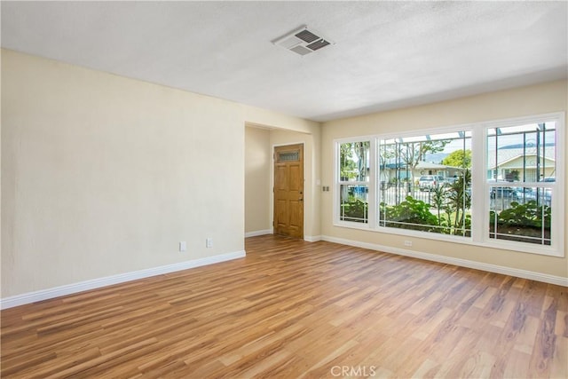 empty room featuring light wood finished floors, visible vents, and baseboards