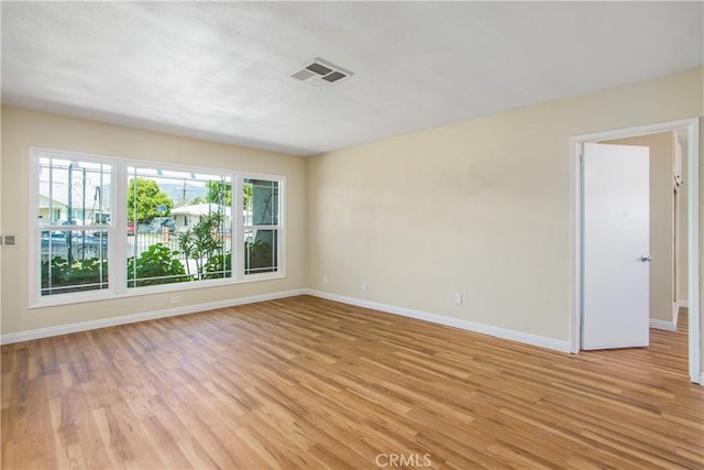 empty room featuring light wood-style floors, visible vents, and baseboards