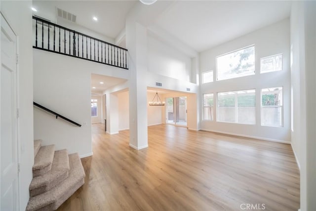 unfurnished living room featuring baseboards, stairway, a high ceiling, visible vents, and light wood finished floors
