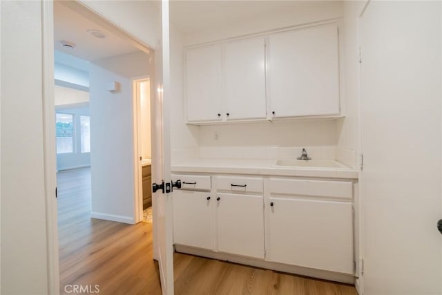 bar with a sink, light wood-style flooring, and baseboards