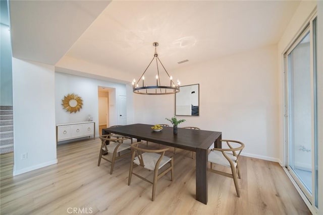 dining area featuring a chandelier, light wood-type flooring, baseboards, and stairs