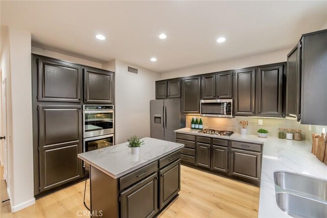 kitchen with light wood-style floors, visible vents, a center island, stainless steel appliances, and decorative backsplash