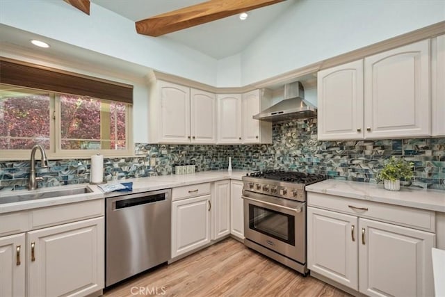 kitchen with wall chimney range hood, a sink, tasteful backsplash, and appliances with stainless steel finishes