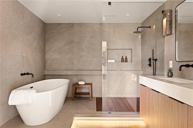 bathroom with a walk in shower, vanity, tile walls, and a soaking tub