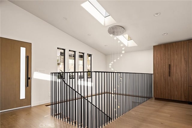 hall featuring vaulted ceiling with skylight, wood finished floors, an upstairs landing, and recessed lighting