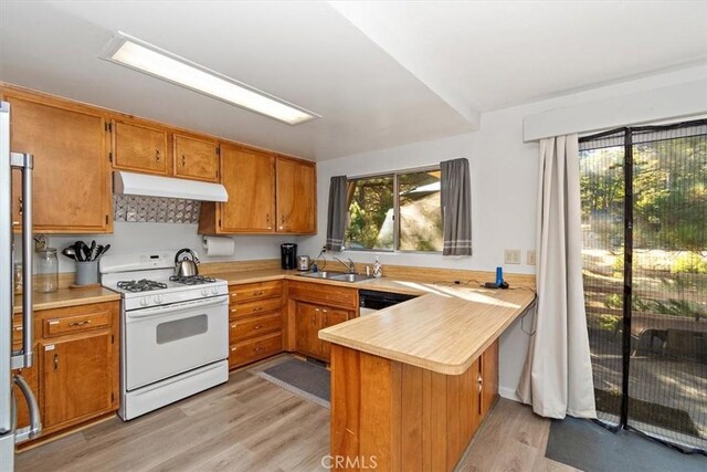 kitchen with light countertops, a sink, white range with gas cooktop, a peninsula, and under cabinet range hood