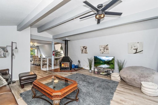 living area with vaulted ceiling with beams, ceiling fan, wood finished floors, and a wood stove