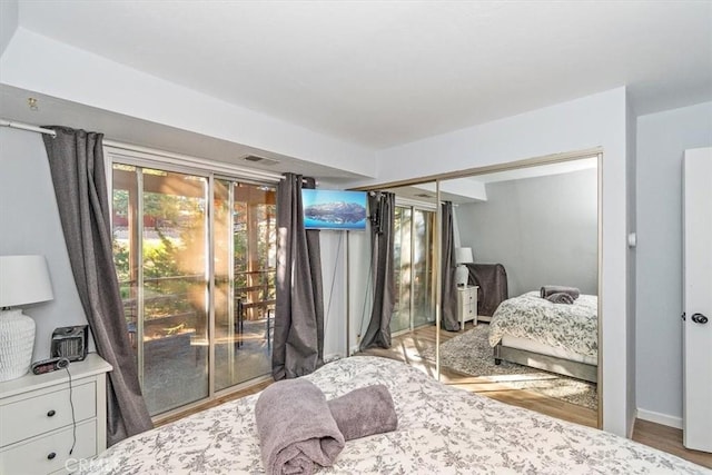 bedroom with baseboards, access to exterior, visible vents, a closet, and wood finished floors