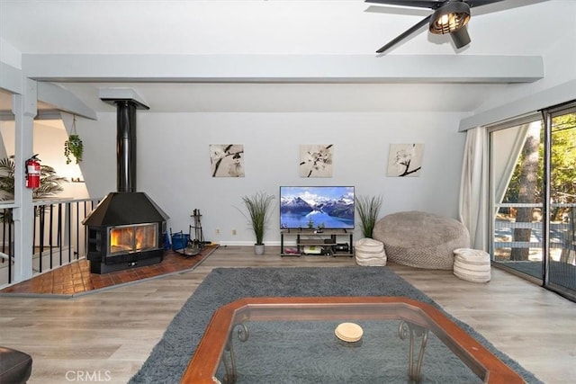 living area featuring a wood stove, baseboards, beamed ceiling, ceiling fan, and wood finished floors
