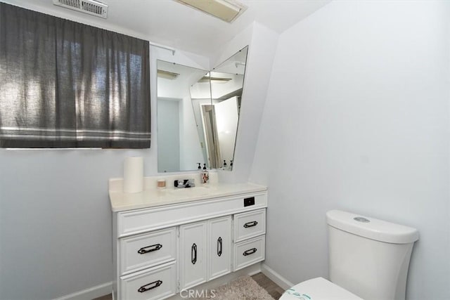 half bath featuring toilet, vanity, baseboards, and visible vents