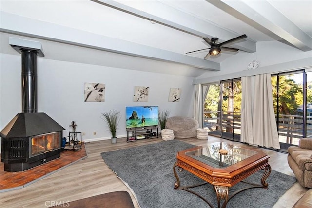 living room with a wood stove, baseboards, ceiling fan, vaulted ceiling with beams, and wood finished floors