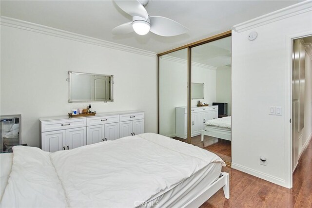 bedroom featuring a closet, crown molding, a ceiling fan, wood finished floors, and baseboards