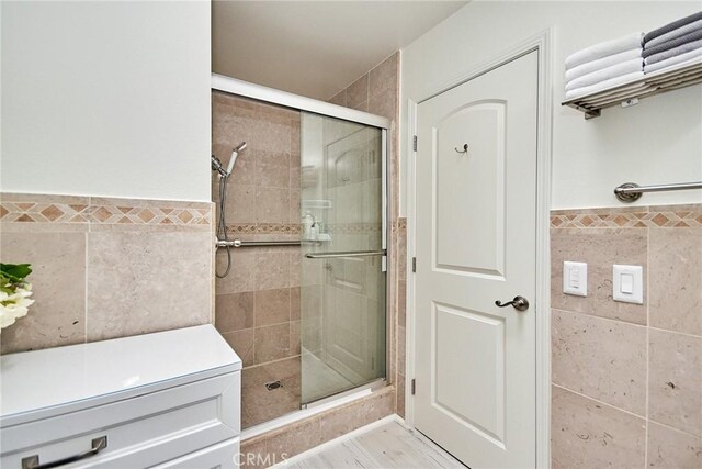 full bathroom with a shower stall, wainscoting, wood finished floors, and tile walls