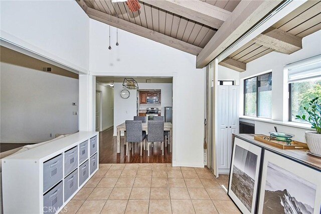 kitchen with stainless steel microwave, lofted ceiling with beams, light tile patterned flooring, wood ceiling, and beverage cooler