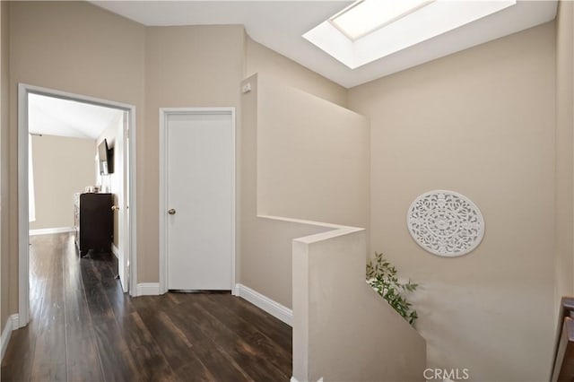hallway featuring baseboards, a skylight, and dark wood-style floors