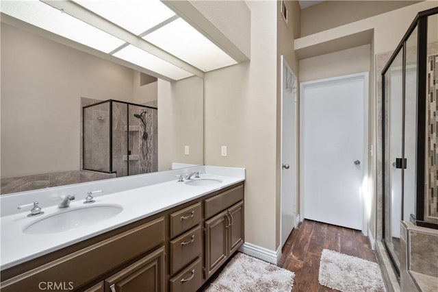 bathroom featuring double vanity, a shower stall, wood finished floors, and a sink