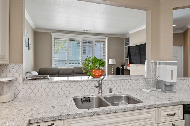 kitchen with a sink, decorative backsplash, ornamental molding, light stone countertops, and visible vents
