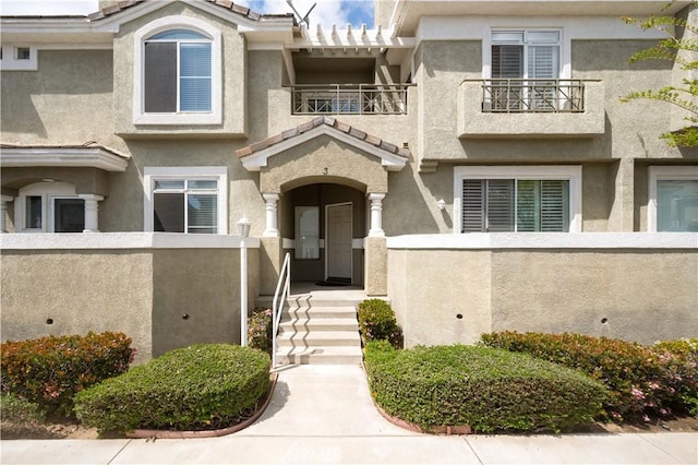 property entrance with stucco siding, a tiled roof, a balcony, and fence