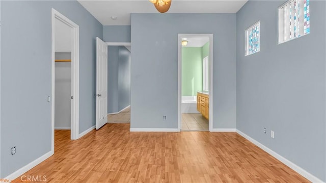 unfurnished bedroom featuring connected bathroom, a closet, a spacious closet, light wood finished floors, and baseboards