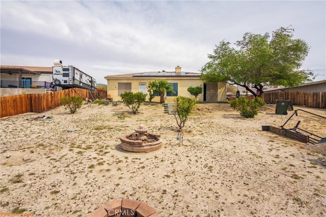 rear view of property featuring fence, a fire pit, stucco siding, and roof mounted solar panels