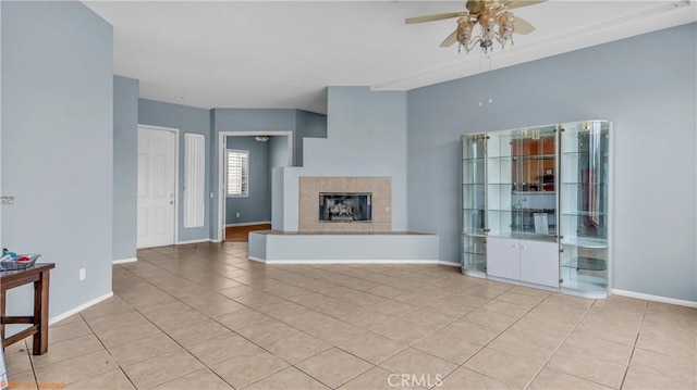 unfurnished living room featuring light tile patterned floors, baseboards, a ceiling fan, and a fireplace