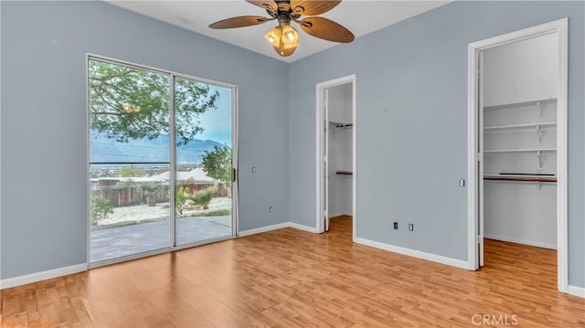 unfurnished bedroom with light wood-style flooring, a spacious closet, access to outside, and baseboards