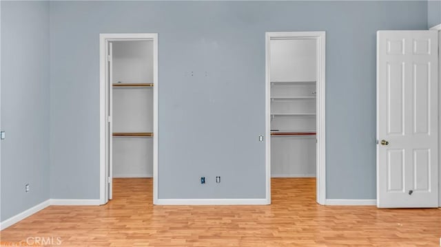 unfurnished bedroom featuring baseboards, a walk in closet, and wood finished floors