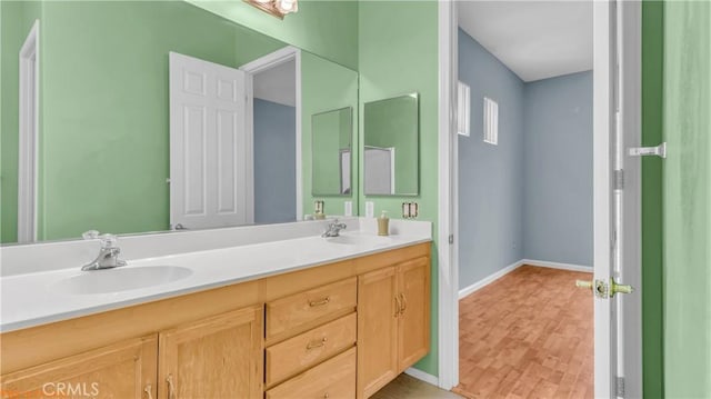 full bath featuring double vanity, baseboards, a sink, and wood finished floors