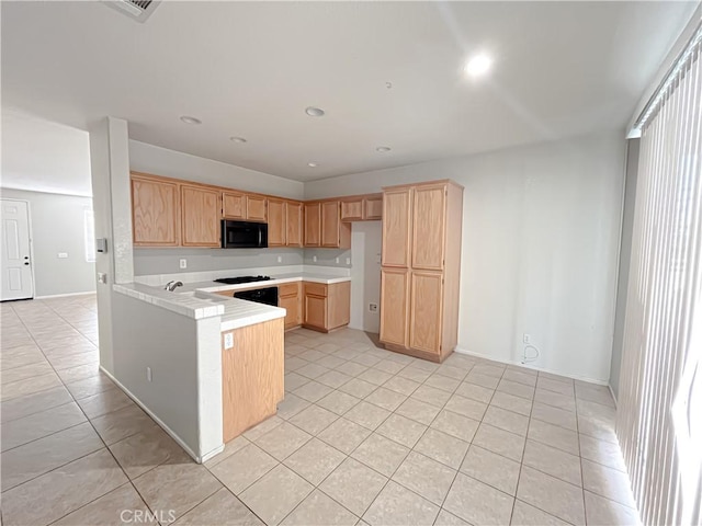 kitchen with light countertops, light brown cabinets, light tile patterned flooring, black microwave, and a peninsula
