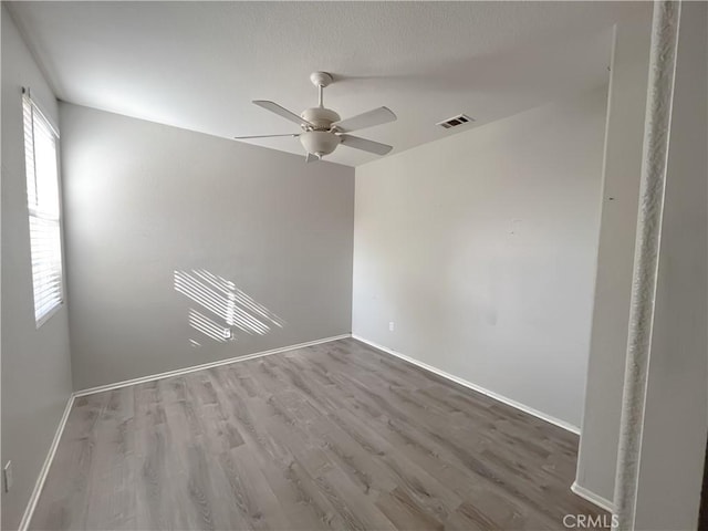 spare room with wood finished floors, baseboards, a ceiling fan, and visible vents