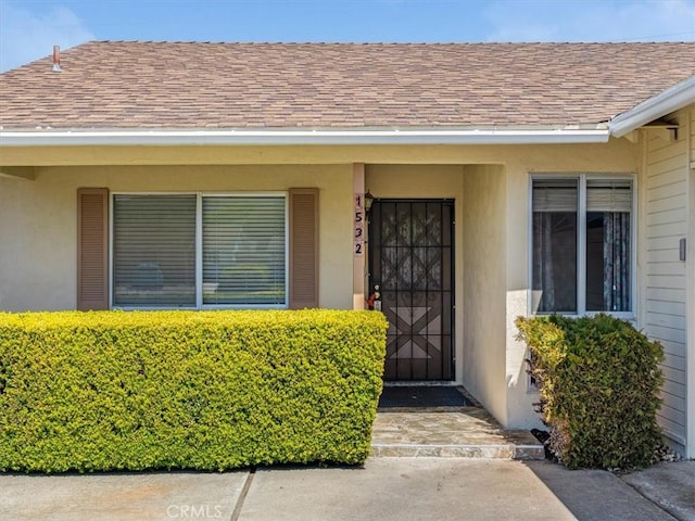 doorway to property featuring stucco siding and a shingled roof