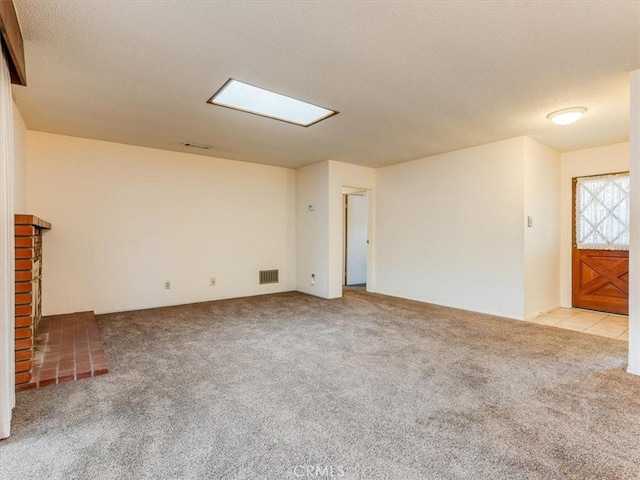 spare room featuring a brick fireplace, light colored carpet, visible vents, and a textured ceiling