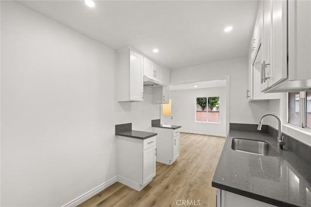 kitchen featuring white cabinets, light wood finished floors, a sink, dark stone counters, and recessed lighting