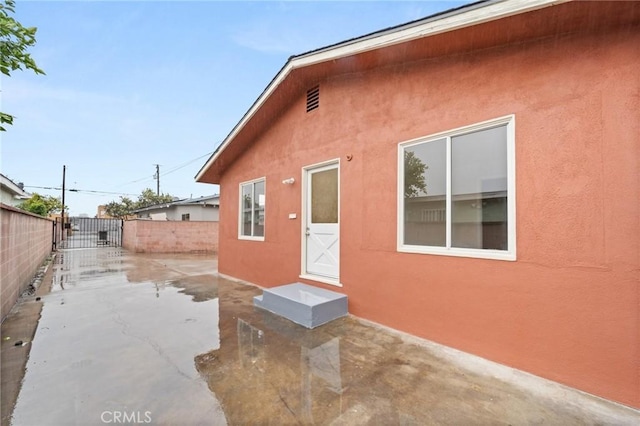 rear view of property with stucco siding, a gate, fence, and a patio area