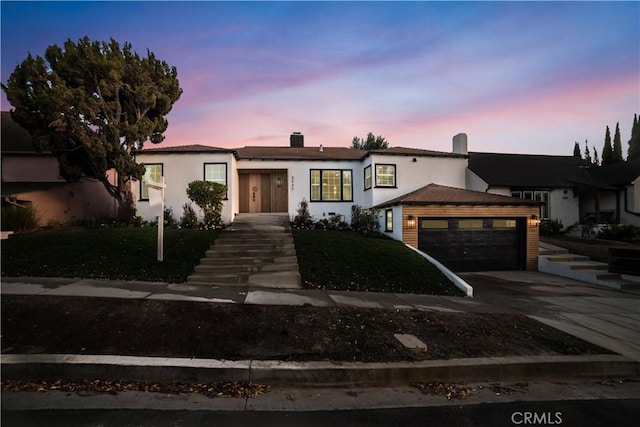 view of front of home featuring stucco siding, driveway, a front lawn, a garage, and a chimney