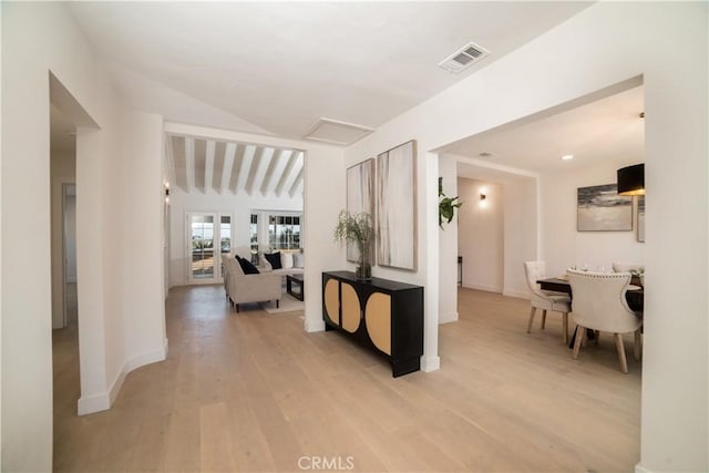 hallway with visible vents, baseboards, attic access, light wood-type flooring, and vaulted ceiling