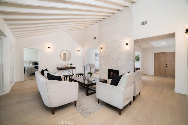 living area featuring high vaulted ceiling, beam ceiling, a fireplace, light wood-type flooring, and visible vents